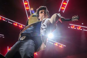 Billie Joe Armstrong playing the guitar behind his head on stage in this low angle shot up.