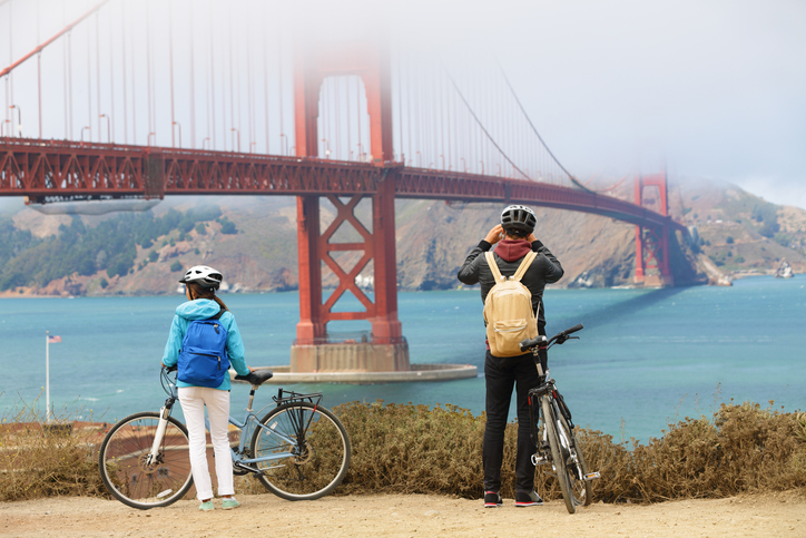 Golden gate bridge - biking couple sightseeing in San Francisco, USA. Young couple tourists on bike tour enjoying the view at the famous travel landmark in California, USA.