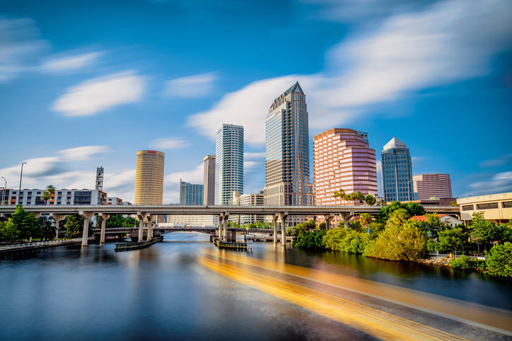 The skyline of downtown Tampa on the Hillsborough river under a blue sky with apartment buildings in the back.